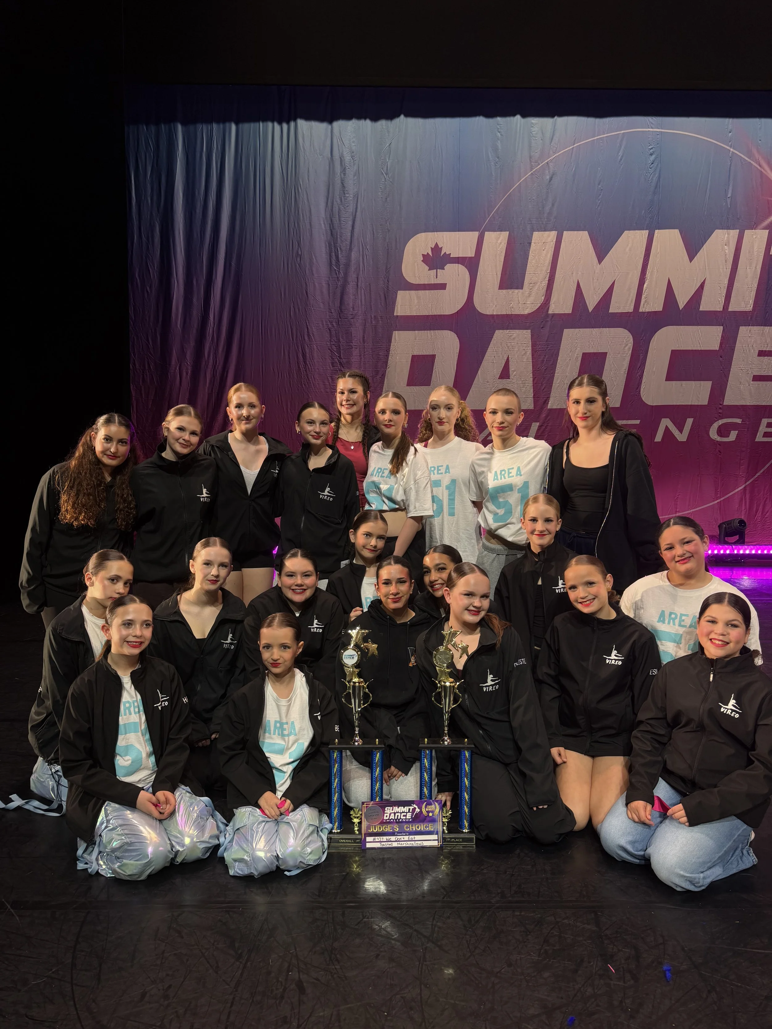 A group of young female dancers on stage holding awards with Summit Dance text on backdrop