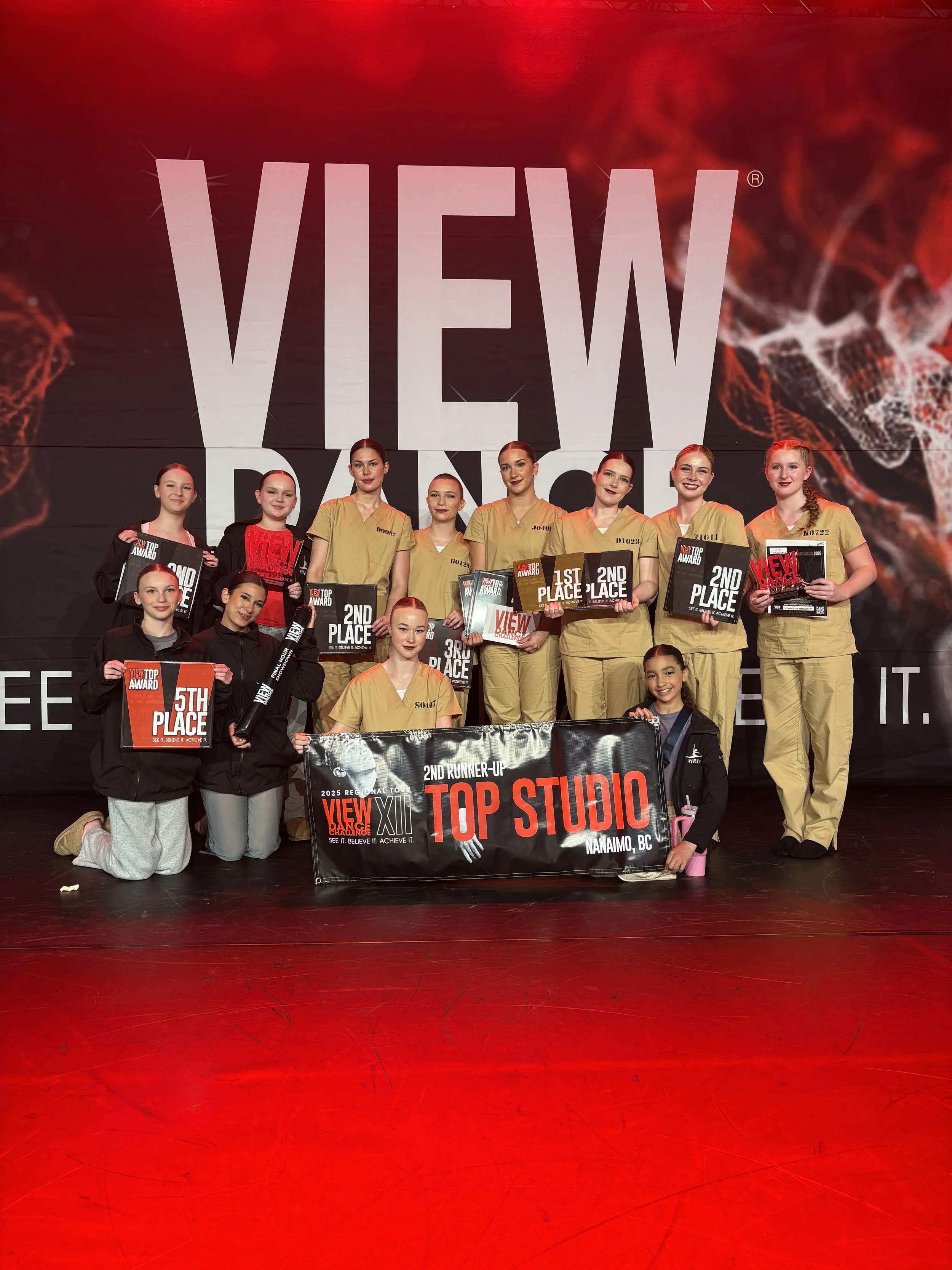 Group of young dancers on stage holding awards and a banner reading Top Studio Nanaimo BC after a dance competition