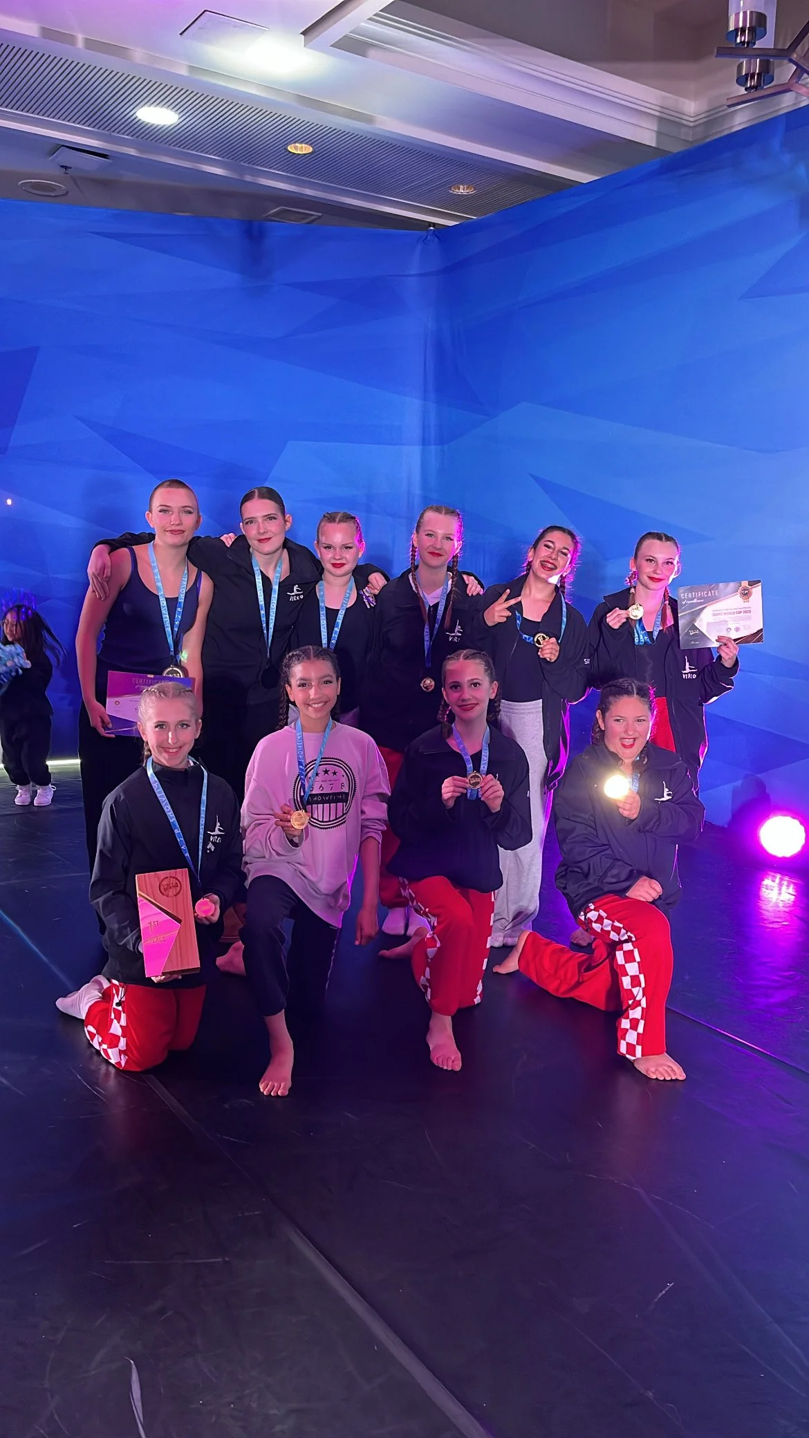 A group of young female dancers with medals and certificates celebrating on stage after a competition